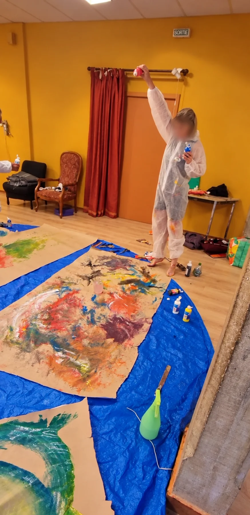 Une participante en combinaison de peintre, debout au-dessus de grandes feuilles étalées au sol