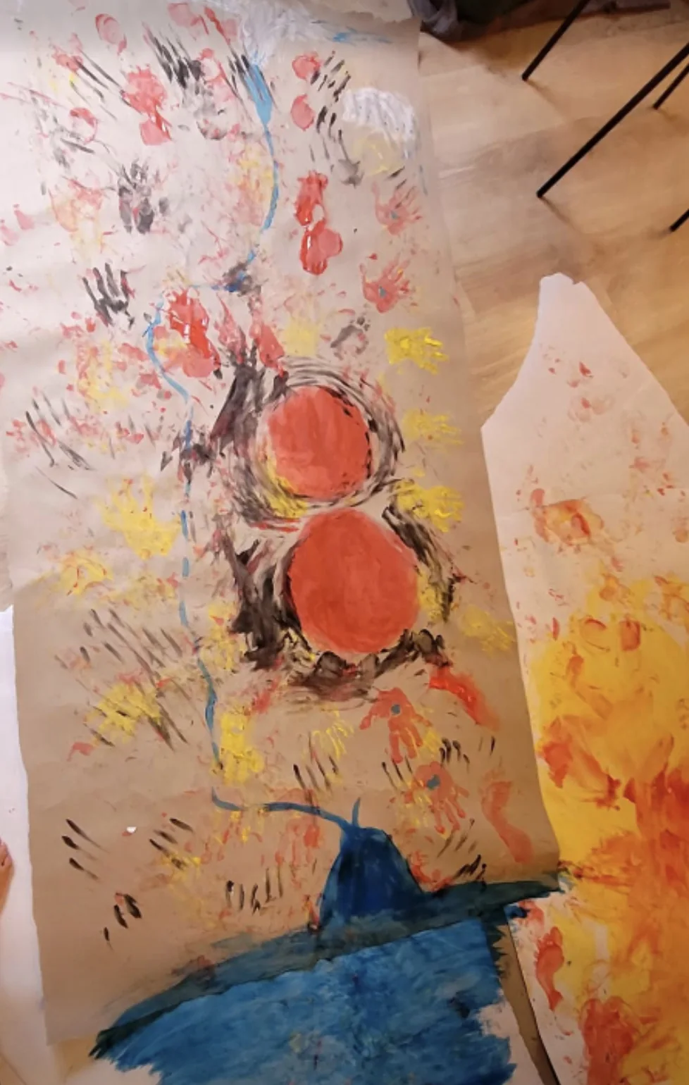 Une grande feuille peinte de mains rouges et jaunes, de deux disques orange et d’un aplat bleu